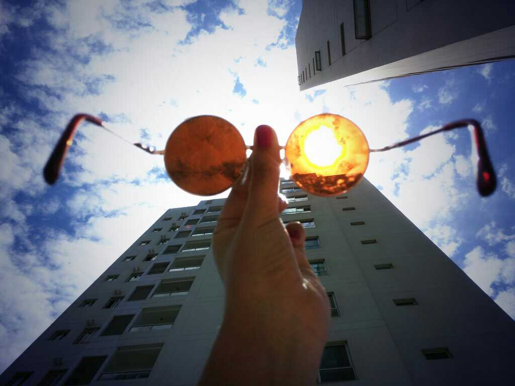 hand holding round sunglasses to the sky in the city